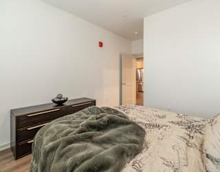 A bedroom with a bed, a dresser, and a doorway leading to another room.