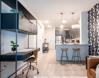 a home office with a desk and stools next to a kitchen with a breakfast bar