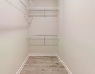a walk in closet with two shelves and a wood floor