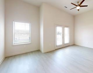A spacious room with a ceiling fan and two windows.
