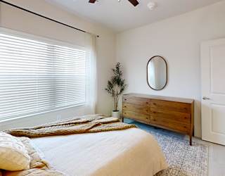 A bedroom with a bed, dresser, and window with blinds.