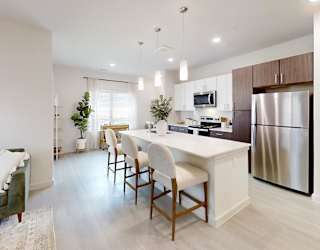 A modern kitchen with a green couch and wooden chairs.