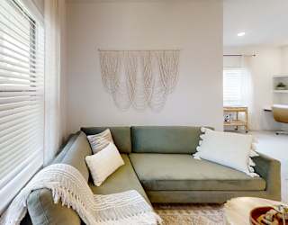 A living room with a green couch and a white wall hanging.