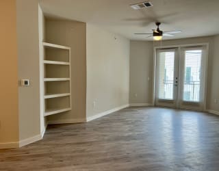 an empty living room with a bookshelf and a ceiling fan