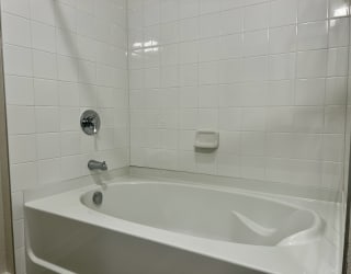 a white bathtub in a white tiled bathroom