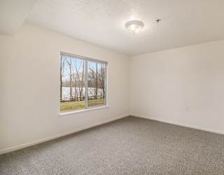 A bedroom with a window and a carpeted floor at Brentwood Park Apartments in LaVista, NE