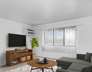 A garden style living room with a grey couch, a coffee table, a television, and a plant at Concord Place Apartments in Kalamazoo, Michigan 49009