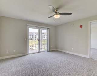 A living room with a ceiling fan and carpeted floor leading to a private balcony at Copper Creek Apartment Homes, Maize, Kansas