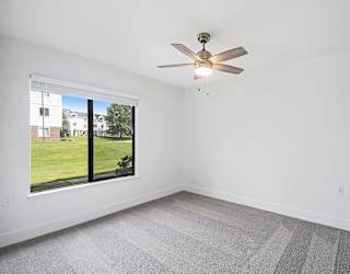 A bedroom with a ceiling fan and a window overlooking a green lawn at The Crossings Apartments in Grand Rapids, MI