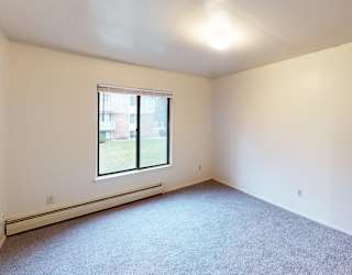 A spacious bedroom with a window and a carpeted floor at Glen Oaks Apartments, Michigan, 49442