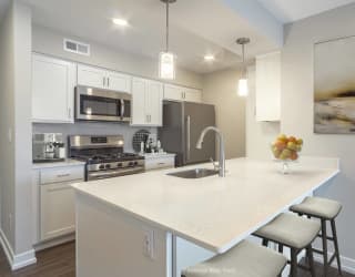 a kitchen with white cabinets and a white island with two stools at Hillside Apartments, Wixom, MI