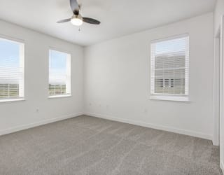 an empty living room with three windows and a ceiling fan at Meadowbrooke Apartment Homes, Michigan