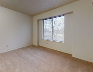 a bedroom with a large window and beige carpeting at Pine Knoll Apartments, Battle Creek, MI