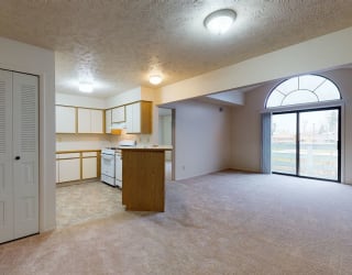an empty living room with a kitchen and a glass door  at Pine Knoll Apartments, Battle Creek, Michigan