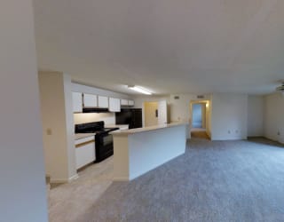 A spacious living room with a kitchen in the background.