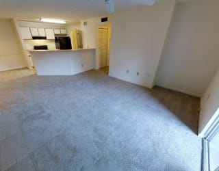 A spacious living room with a kitchen area in the background.