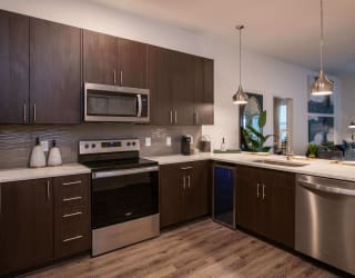 Kitchen with dark wood cabinets, stainless steel appliances, and a built-in beverage cooler at The Apex at CityPlace, Overland Park