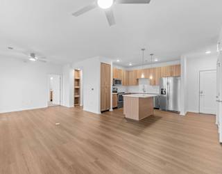 A spacious room with wooden flooring and a kitchen area in the background.