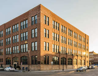 A large red brick building with many windows and cars parked in front.