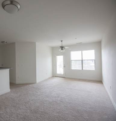an empty living room with a kitchen in the background