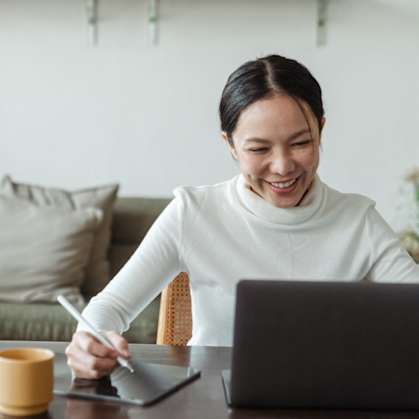 a woman sitting at a table with a laptop and a tablet