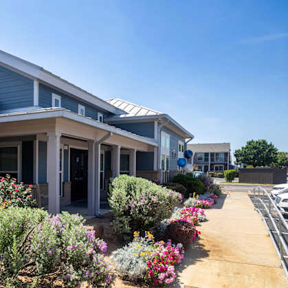 A building with a blue roof and white columns is surrounded by a variety of colorful flowers.