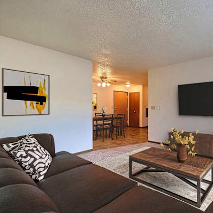 Fargo, ND Prairiewood Courts Apartments.  A living room with a couch, coffee table, and a tv. the dining room is in the background.