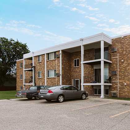 a brick apartment building with two cars parked in a parking lot