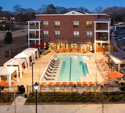 an aerial view of a resort style swimming pool with orange lounge chairs and white umbrellas at The Flats at Southlawn Apartments, Georgia