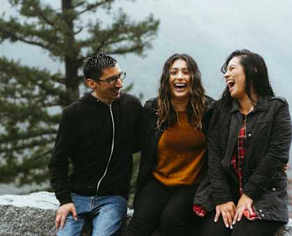 Three people are sitting on a stone wall.