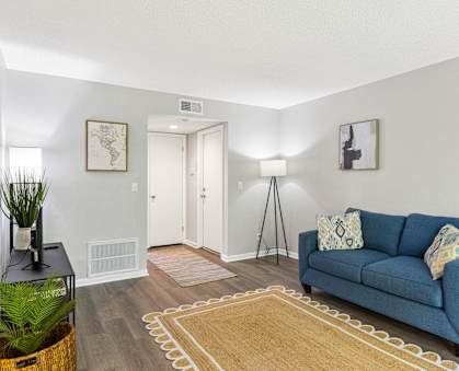 A blue couch with a white pillow is in the middle of a room with a rug on the floor at The Preserve at Pine Valley Apartments, Wilmington, NC