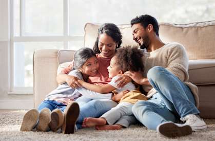 a family of four sits on the floor in front of a couch