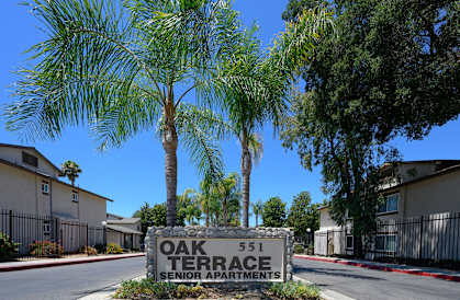 a sign that reads oak terrace senior apartments in front of palm trees