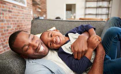 A man is holding a child on his lap while they both smile.
