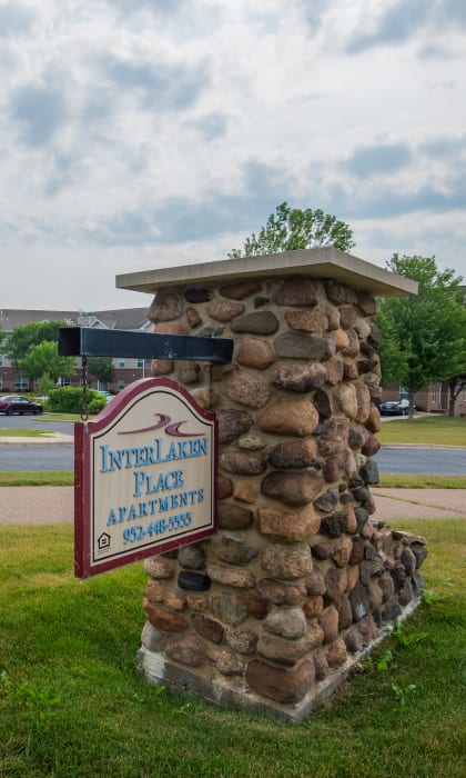 a stone sign in the grass in front of a parking lot