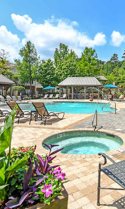 our resort style pool is surrounded by chairs and umbrellas