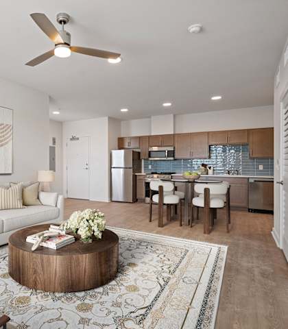 A modern living room with a white sofa, a wooden coffee table, and a dining area in the background.
