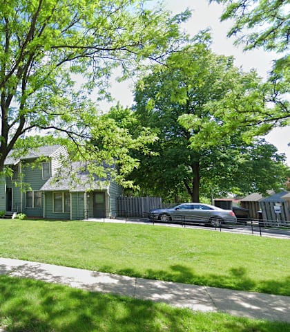 A tree in front of a house with a car parked in the driveway.