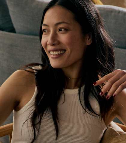 A woman with long dark hair is sitting on a grey couch.