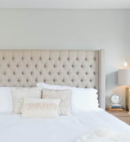 a bedroom with white bedding and a tan tufted headboard