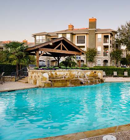 A swimming pool in front of a building with a tree to the right.