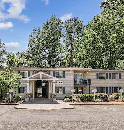 the front of a building with a driveway and trees