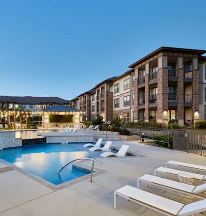 A swimming pool surrounded by lounge chairs and apartment buildings.
