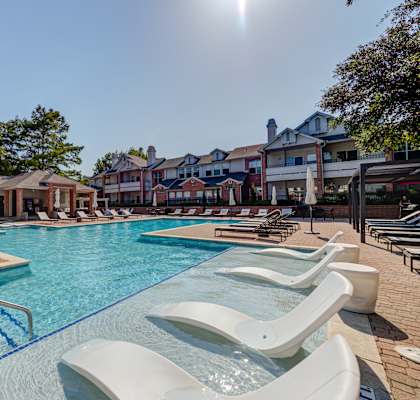 A sunny day at the pool with lounge chairs and a building in the background.