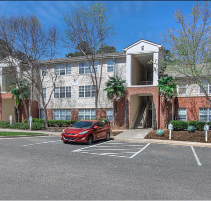 A red car is parked in a parking lot in front of a building.