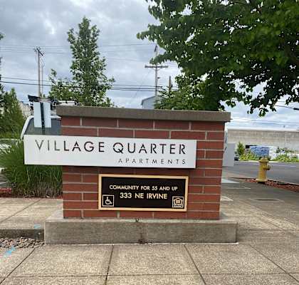 A sign for Village Quarter Apartments sits on a sidewalk.