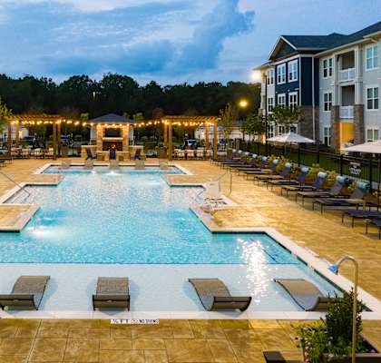 a large pool with lounge chairs and umbrellas in front of an apartment building  at Promenade at Newnan Crossing, Newnan