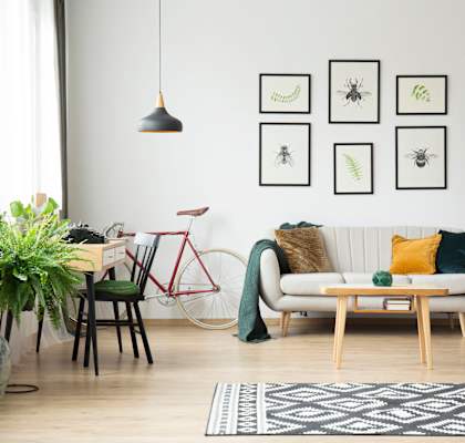 A living room with a white couch, a red bicycle, a wooden table, and a bookshelf with various items.
