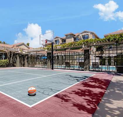 a basketball court in a fenced in backyard with a ball on it