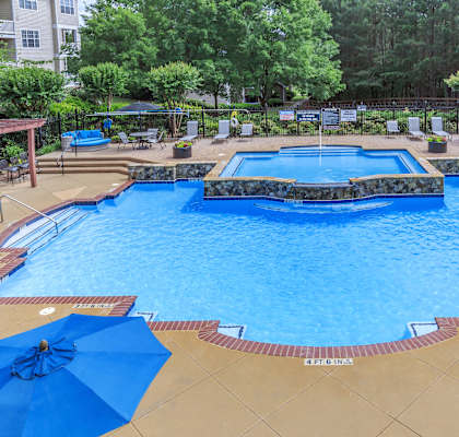 a swimming pool with umbrellas and chairs and trees in the background